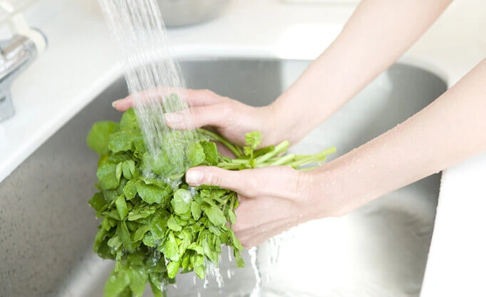 a pair of hands washing vegetables with water