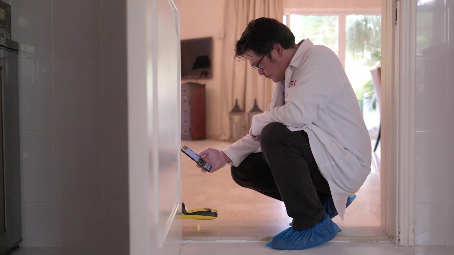 Taking a termite reading at a villa door frame, technician wearing shoe covers indoors